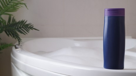 Purple bottle of bubble bath on tub indoors, space for text