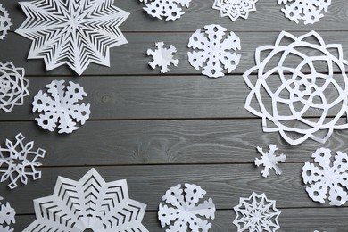 Many paper snowflakes on grey wooden background, flat lay. Space for text