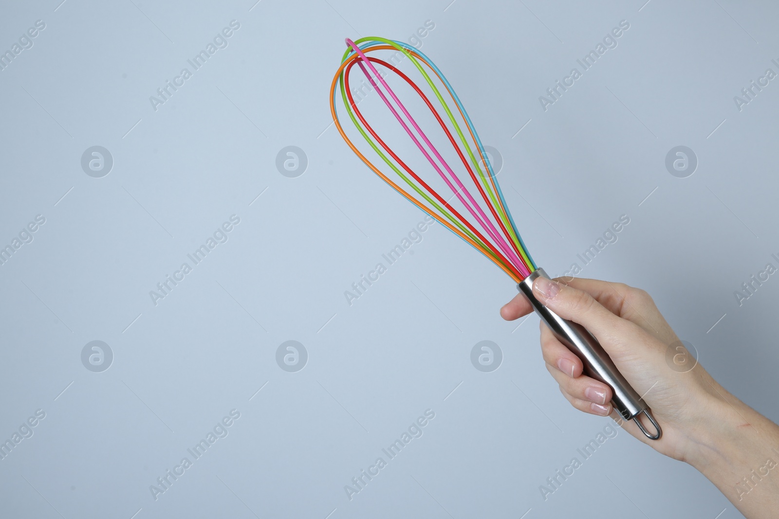 Photo of Woman holding colorful whisk on light grey background, closeup. Space for text