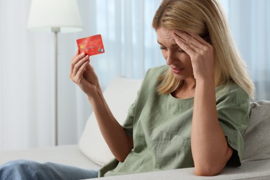 Photo of Stressed woman with credit card on sofa at home. Be careful - fraud