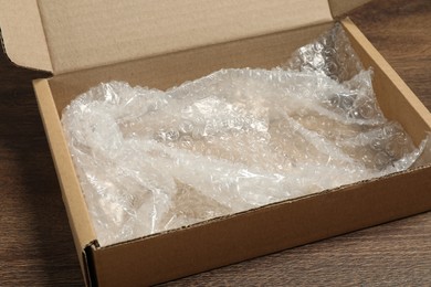 One open cardboard box with bubble wrap on wooden table, closeup