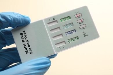 Photo of Doctor holding multi-drug screen test on beige background, closeup