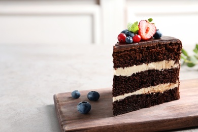 Photo of Wooden board with slice of chocolate sponge berry cake on grey table