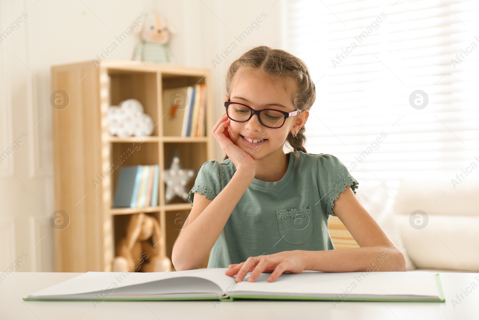 Photo of Cute little girl reading book at desk in room