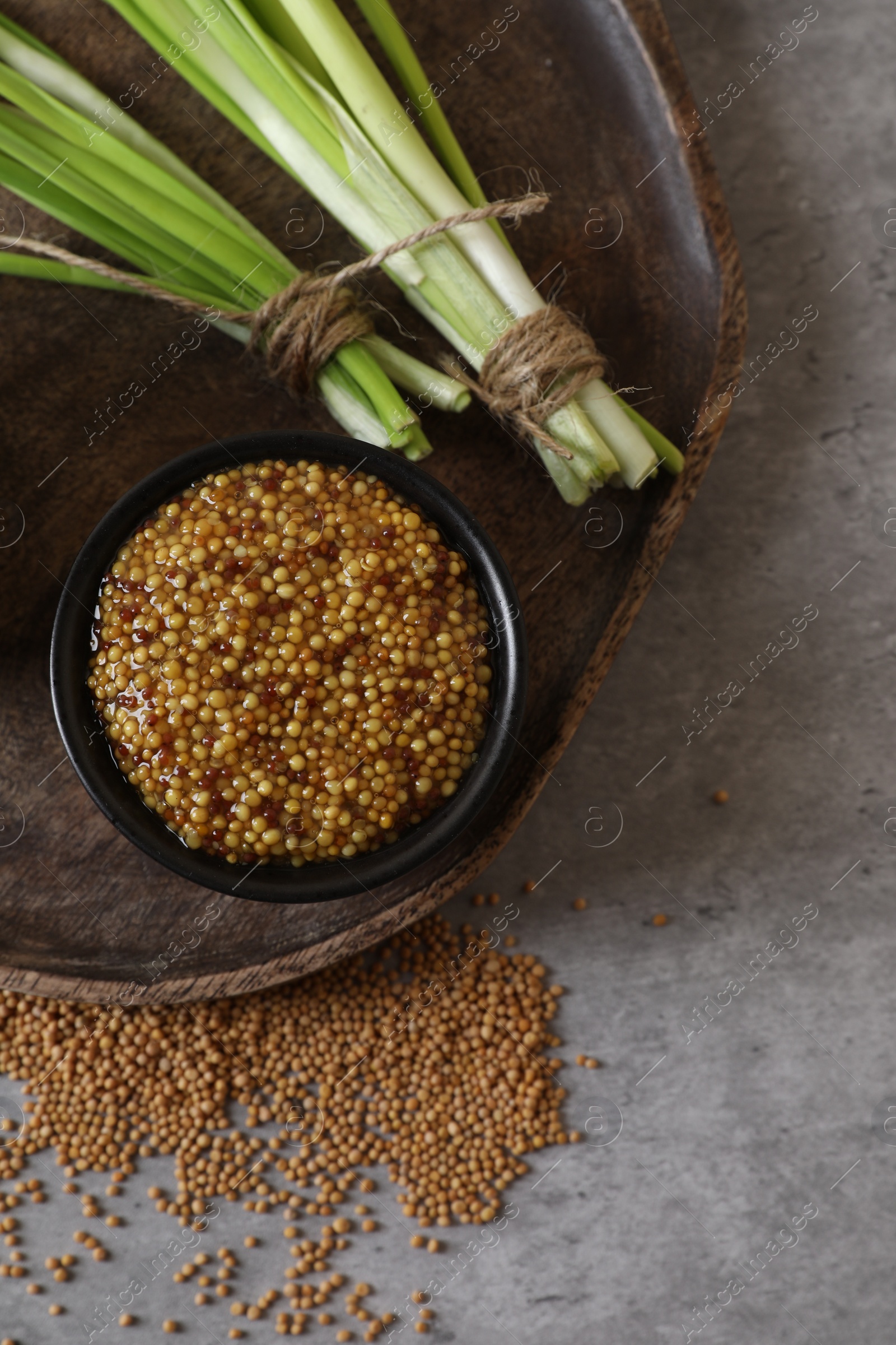 Photo of Serving board with delicious whole grain mustard, seeds and fresh green onion on grey table, top view