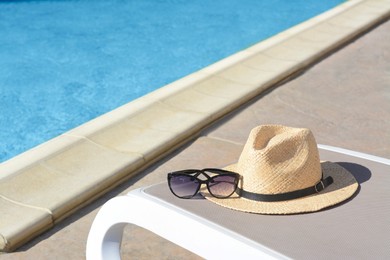 Stylish straw hat and sunglasses on grey sunbed at poolside. Beach accessories