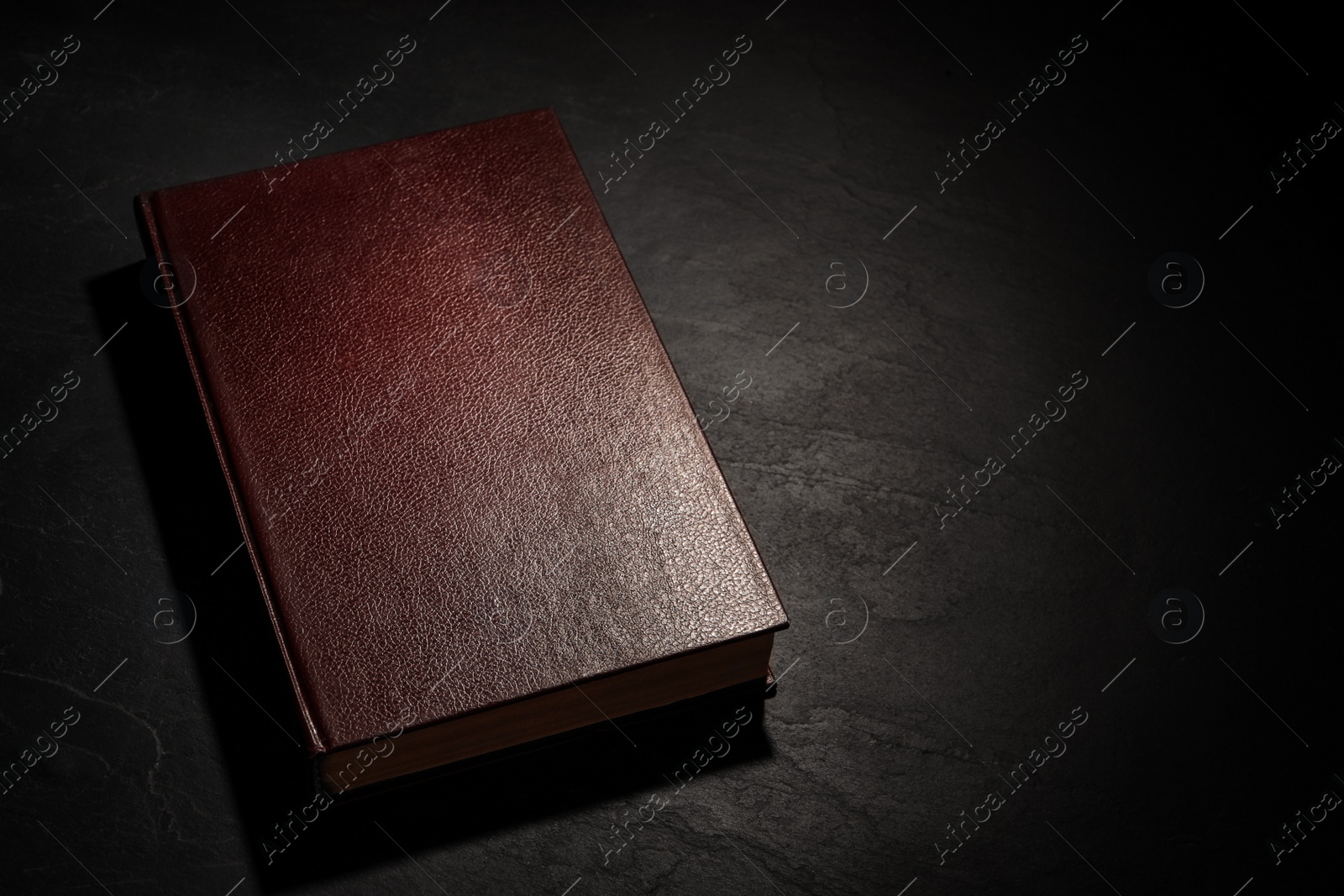 Photo of Old hardcover book on black textured table, space for text