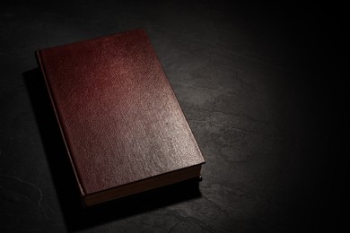 Photo of Old hardcover book on black textured table, space for text