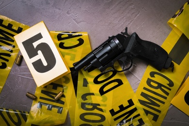 Flat lay with yellow tape, crime scene marker and gun on grey stone background