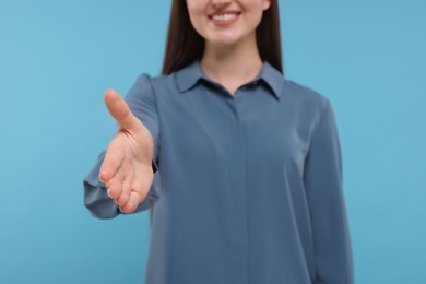 Photo of Smiling woman welcoming and offering handshake on light blue background, closeup