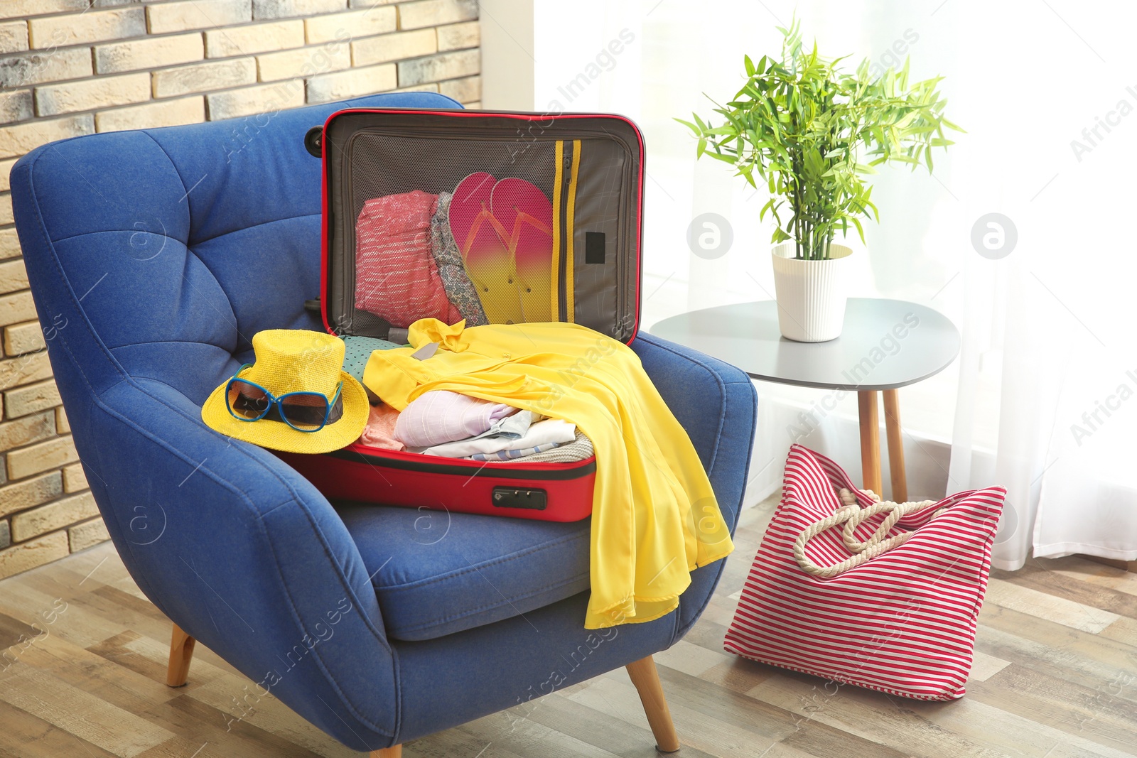 Photo of Open suitcase with different clothes and accessories for summer journey on armchair