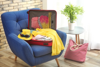 Photo of Open suitcase with different clothes and accessories for summer journey on armchair