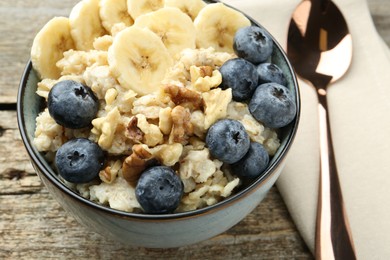 Tasty oatmeal with banana, blueberries and walnuts served in bowl on wooden table, closeup