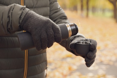 Man pouring drink from thermos into cap outdoors, closeup