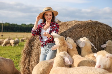 Photo of Smiling woman and sheep near hay bale on animal farm