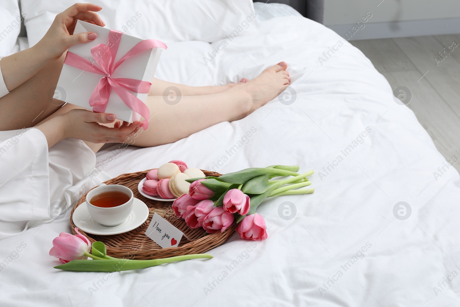 Photo of Tasty breakfast served in bed. Woman with gift box, tea, macarons, flowers and I Love You card at home, closeup. Space for text