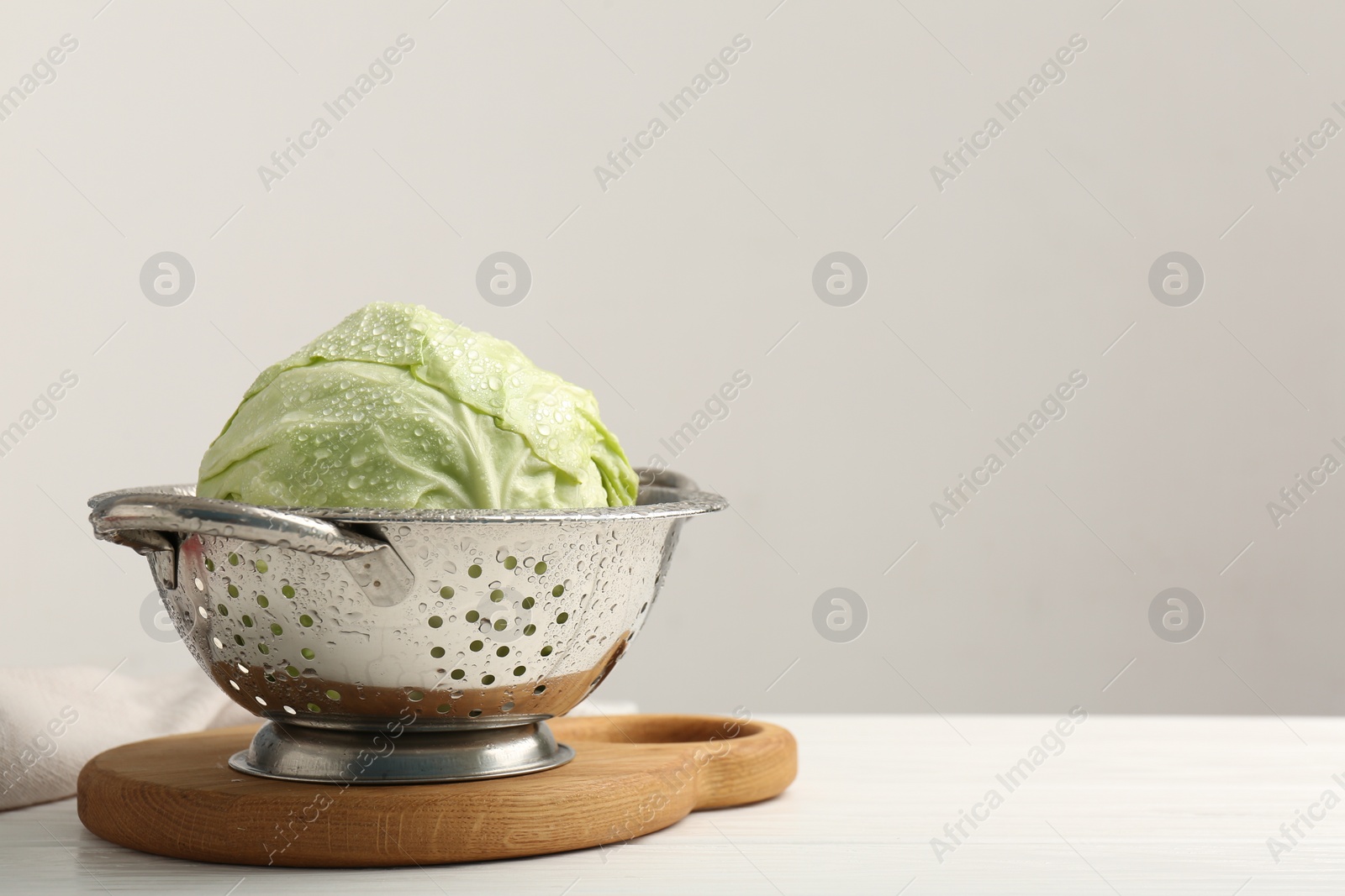 Photo of Wet cabbage in colander on white wooden table. Space for text