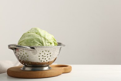 Photo of Wet cabbage in colander on white wooden table. Space for text