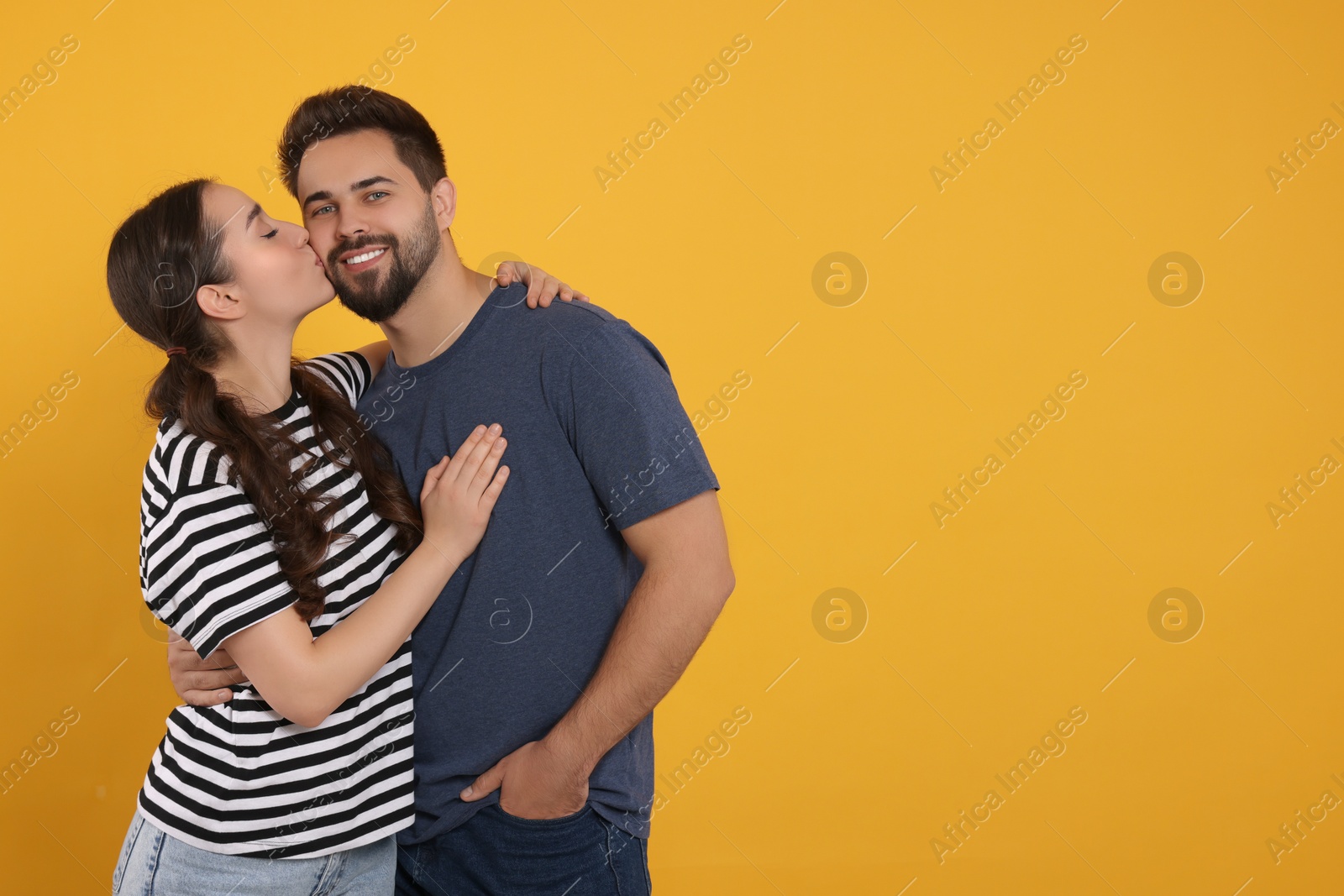 Photo of Woman kissing her smiling boyfriend on orange background. Space for text