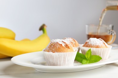 Tasty muffins served with mint on white table, closeup