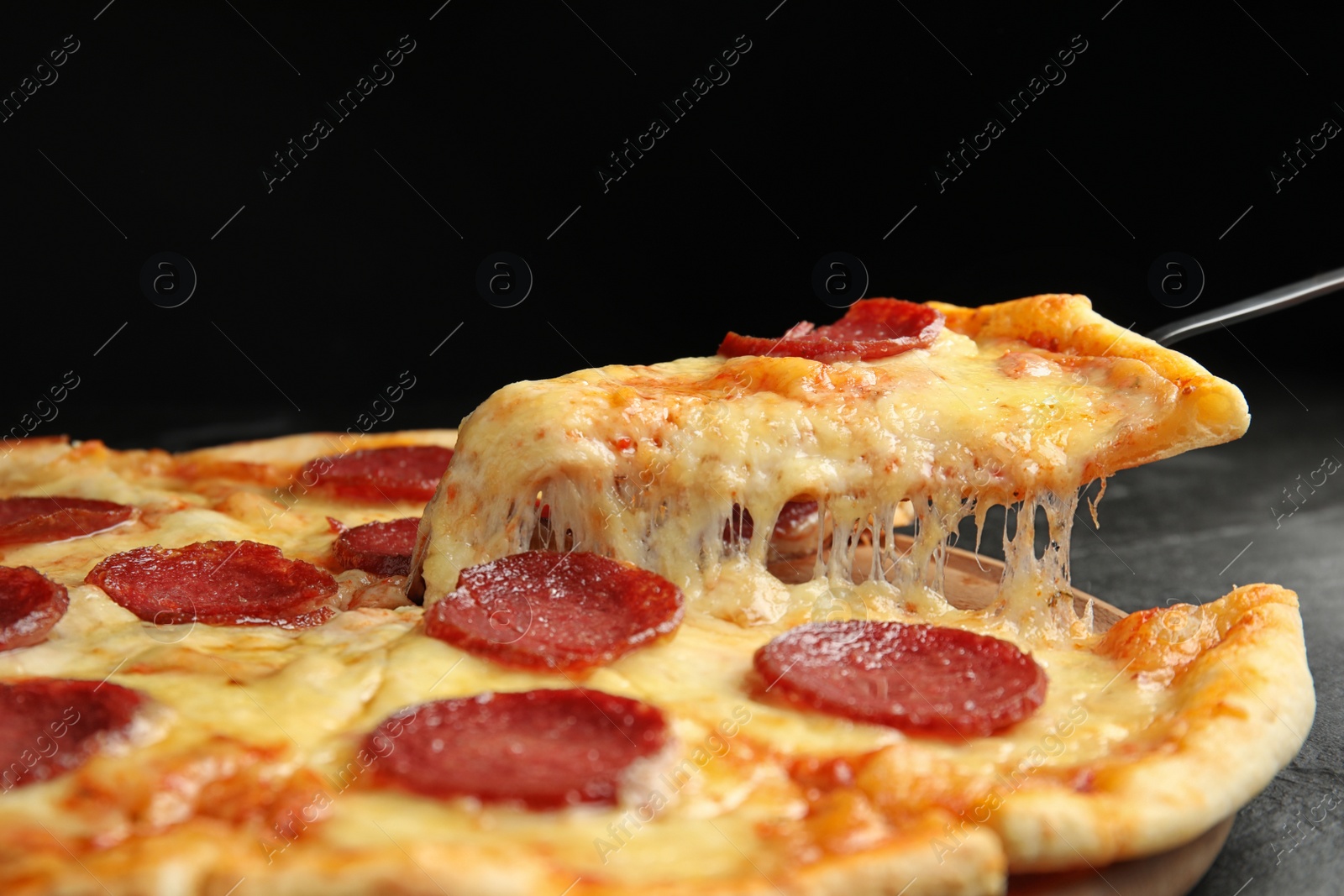 Photo of Taking slice of tasty pepperoni pizza on black table, closeup