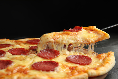 Taking slice of tasty pepperoni pizza on black table, closeup