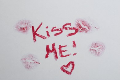 Photo of Phrase Kiss Me, marks and red heart made with lipstick on white background, above view