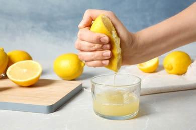 Photo of Woman squeezing lemon juice into glass on table