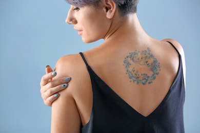 Young woman with tattoo on color background