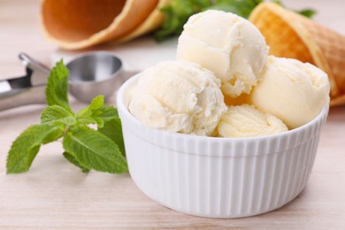 Bowl of ice cream and mint leaves on light wooden table, closeup