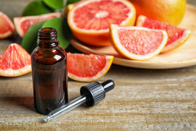 Photo of Citrus essential oil and grapefruits on wooden table. Space for text