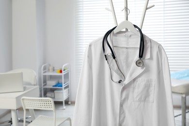 Photo of White doctor's gown and stethoscope on rack in clinic. Space for text