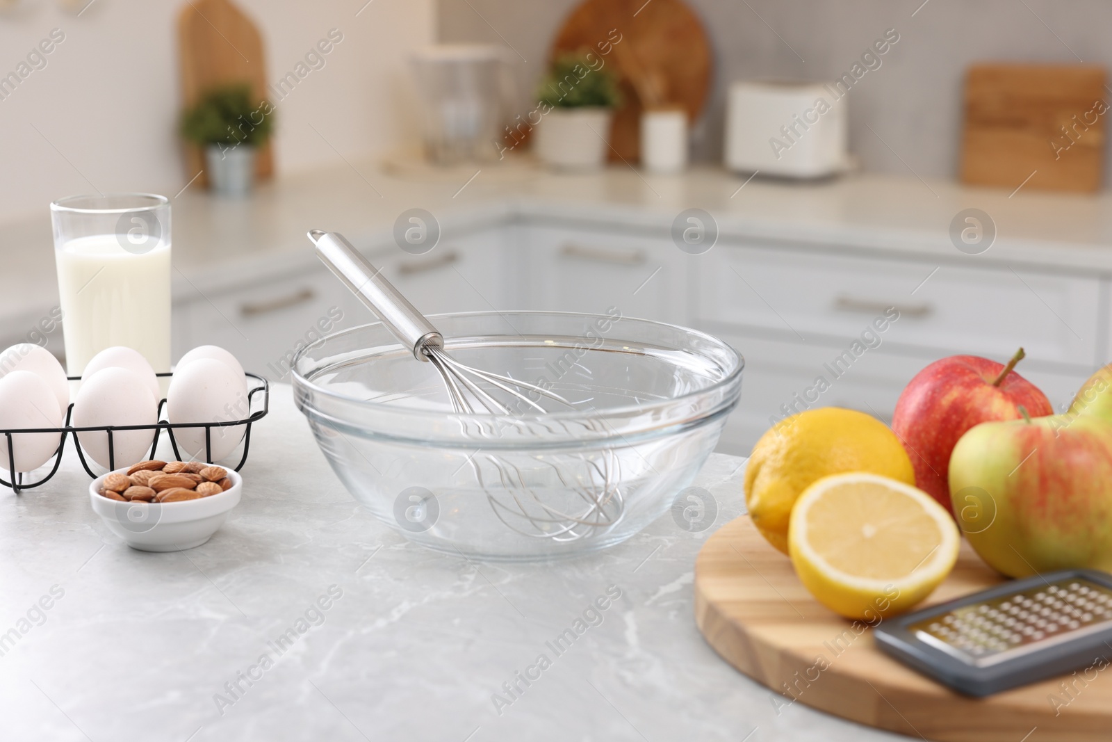 Photo of Metal whisk, bowl, grater and different products on gray marble table in kitchen