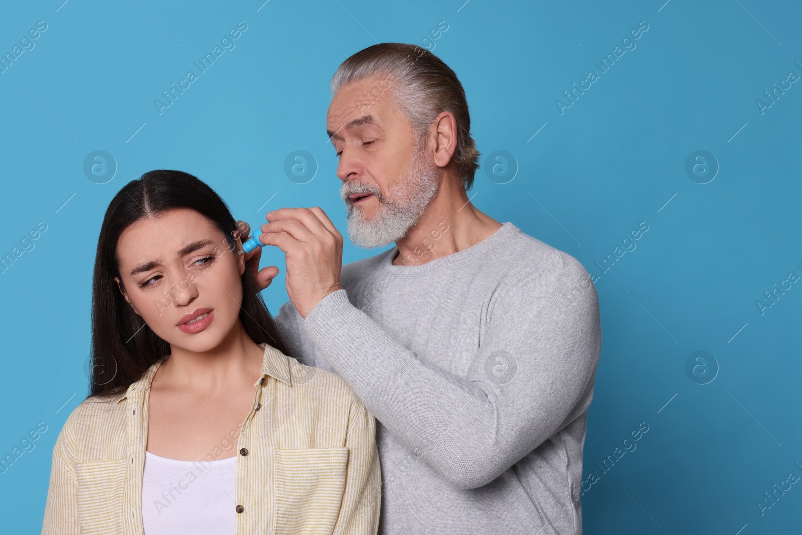 Photo of Senior man dripping medication into woman's ear on light blue background, space for text