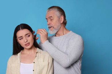 Senior man dripping medication into woman's ear on light blue background, space for text