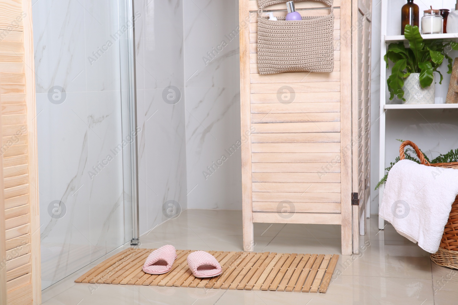 Photo of Wooden mat with slippers on floor in bathroom