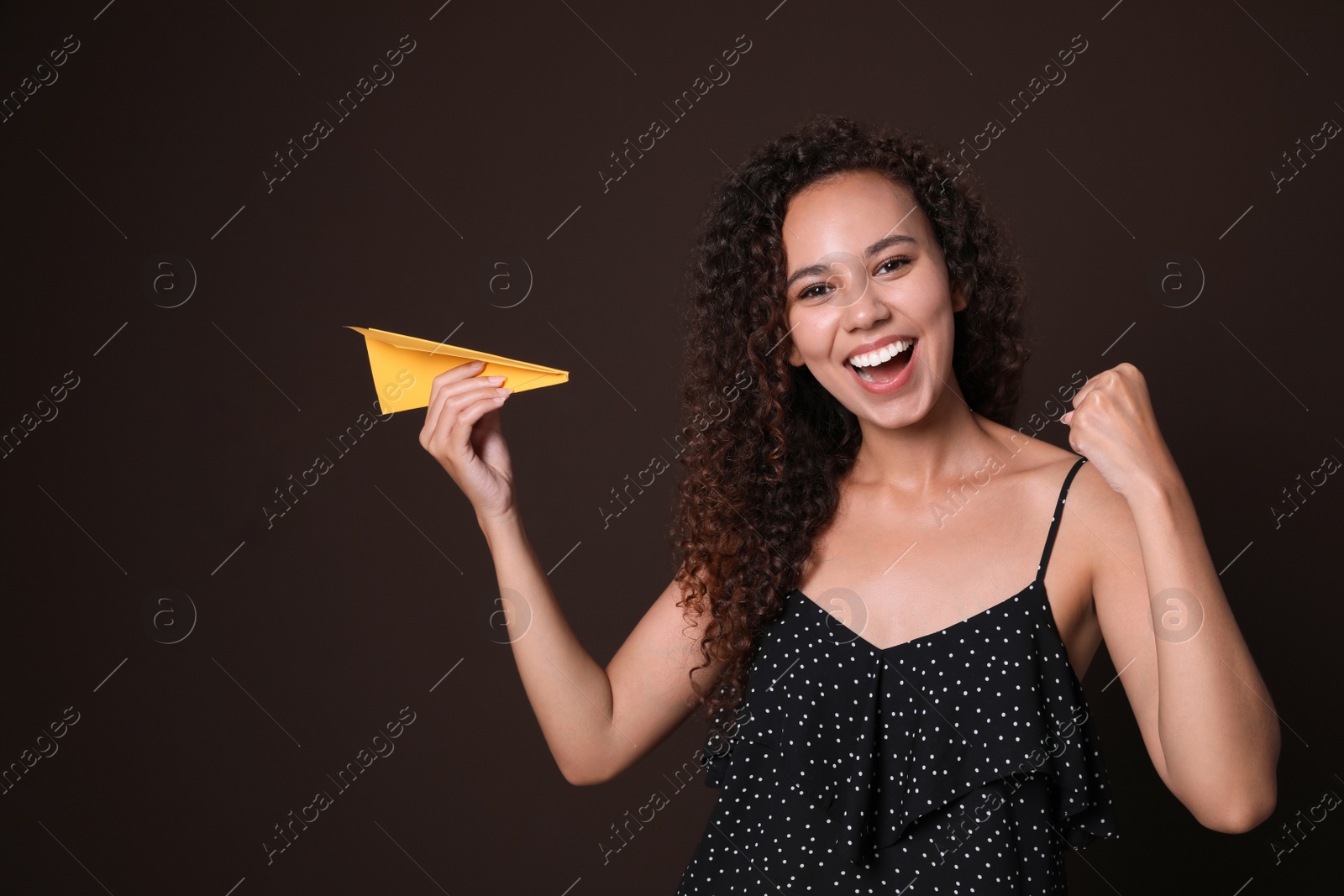 Photo of Beautiful African-American woman playing with paper plane on brown background