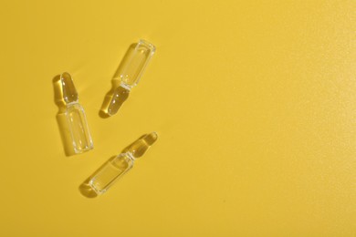 Glass ampoules with liquid on yellow background, flat lay. Space for text