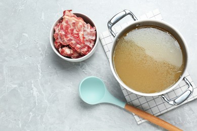 Pot with delicious broth and bowl of bones on light grey table, flat lay. Space for text