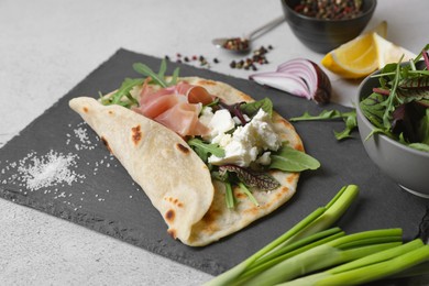 Delicious pita wrap with jamon, cheese cream and greens on light gray table