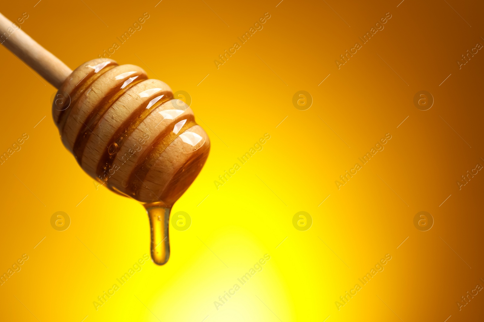 Photo of Pouring honey from dipper against golden background, space for text