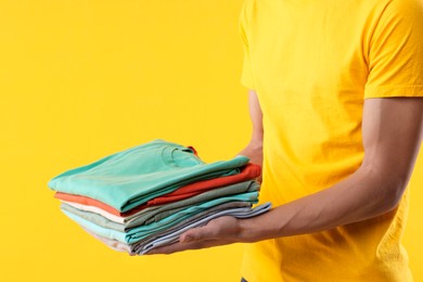 Photo of Dry-cleaning delivery. Courier holding folded clothes on orange background, closeup