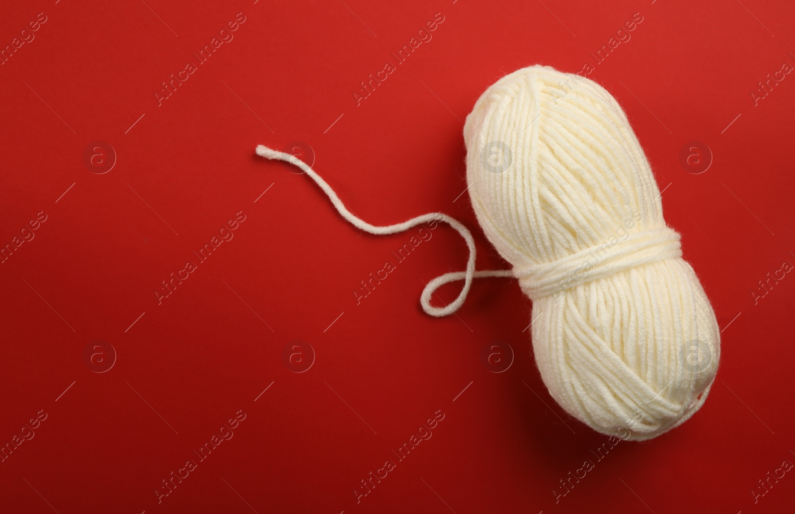 Photo of Soft white woolen yarn on red background, top view. Space for text