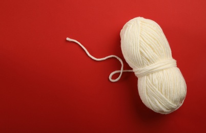 Soft white woolen yarn on red background, top view. Space for text