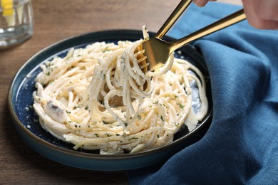 Photo of Eating delicious pasta with mushroom sauce at wooden table, closeup