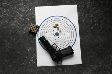 Photo of Shooting target, handgun and bullets on dark gray table, top view