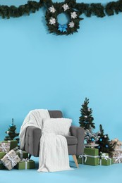 Photo of Beautiful Christmas themed photo zone with stylish armchair, trees and gift boxes on light blue background
