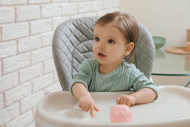 Cute little baby sitting in high chair indoors