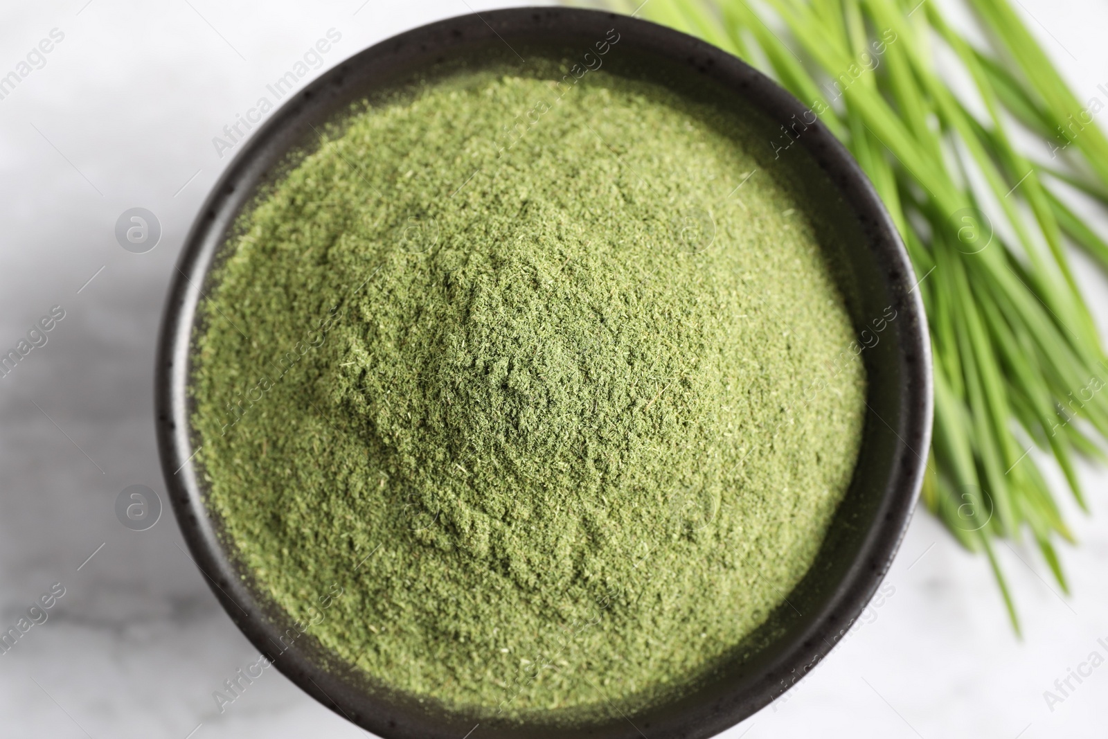 Photo of Wheat grass powder in bowl on white table, top view