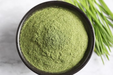 Wheat grass powder in bowl on white table, top view